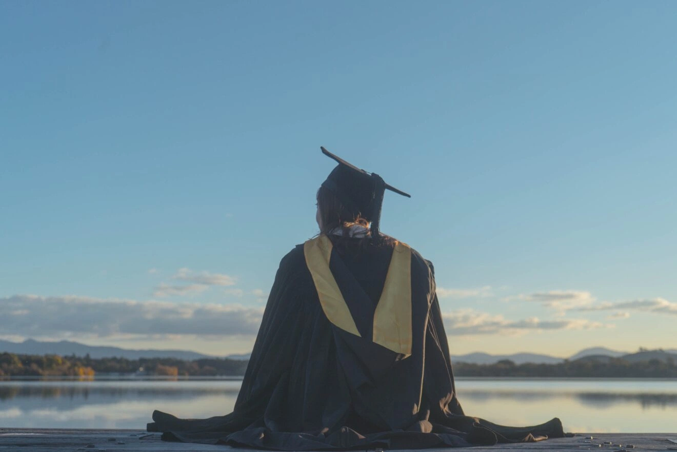 Graduate in cap and gown on the banks of Lake Burley Griffin, Canberra. Photo by Zayneyee Liew on Pexels.